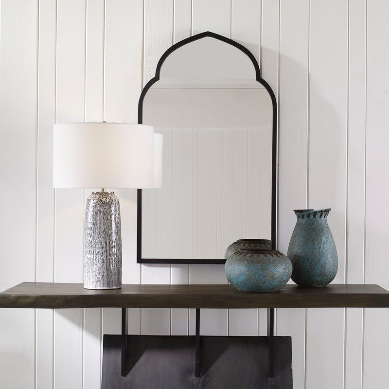 Uttermost Kenitra arched mirror with a sleek, curved frame, hanging on a wall, showcasing its elegant design and reflective surface.