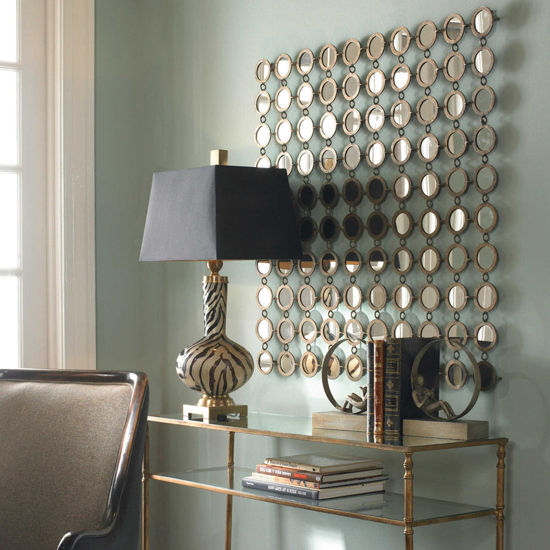 Uttermost Dinuba wall mirror with antique silver champagne finish, decorative frame, hanging on a wall in a stylish interior setting.