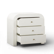 TOV Furniture Hump bedside chest with two drawers and wooden finish, placed beside a bed in a modern bedroom setting.