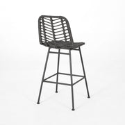Two Noble House Sawtelle outdoor wicker barstools with armrests and cushions, arranged on a patio setting.