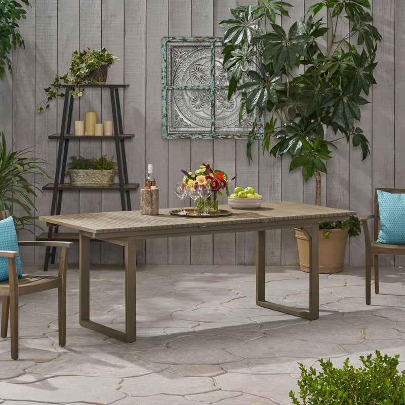 Outdoor expandable acacia wood dining table with U-shaped legs from Noble House, featuring a natural wood finish and sturdy design.