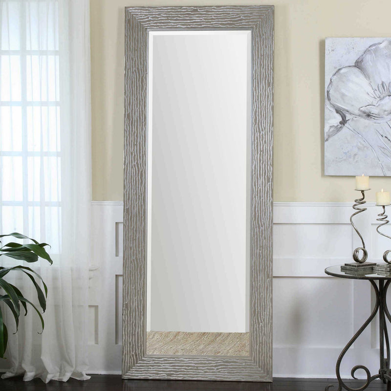 Large silver floor mirror by Uttermost with a sleek, modern frame reflecting surrounding space in a contemporary setting.