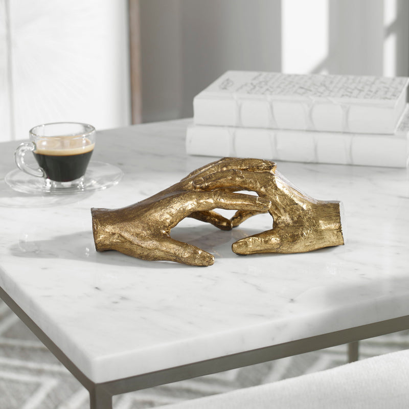 Gold "Hold My Hand" sculpture by Uttermost, featuring a detailed figurine of two hands gently clasped together.