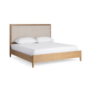 Upholstered bed by Classic Home with plush fabric headboard and sleek wooden legs, shown in a cozy bedroom setting.
