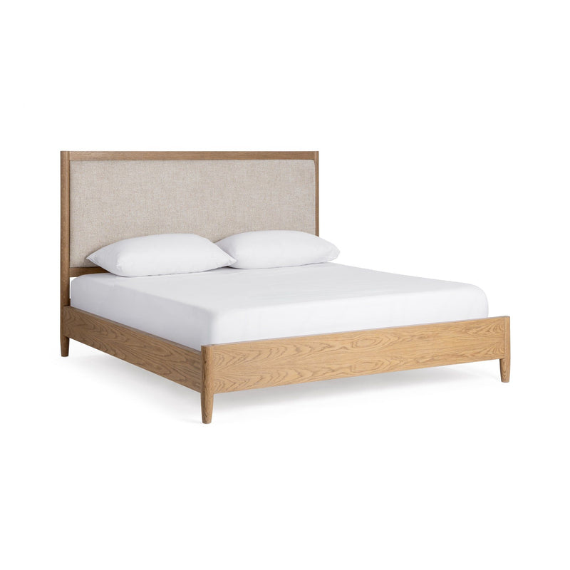 Upholstered bed by Classic Home with plush fabric headboard and sleek wooden legs, shown in a cozy bedroom setting.