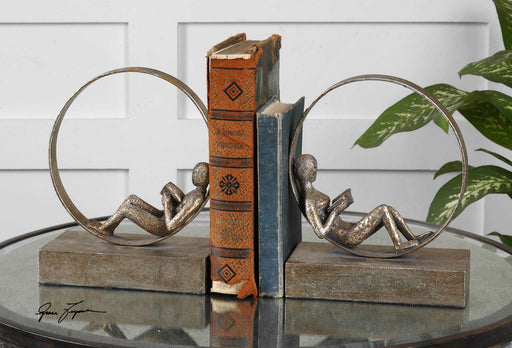 Dark brown Lounging Reader antique bookends set by Uttermost, featuring detailed reclining figure designs on a wooden surface.