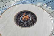 Beige Rainier Ranch round fire pit table by Signature Design Ashley, featuring a spacious tabletop and fire bowl for outdoor gatherings.