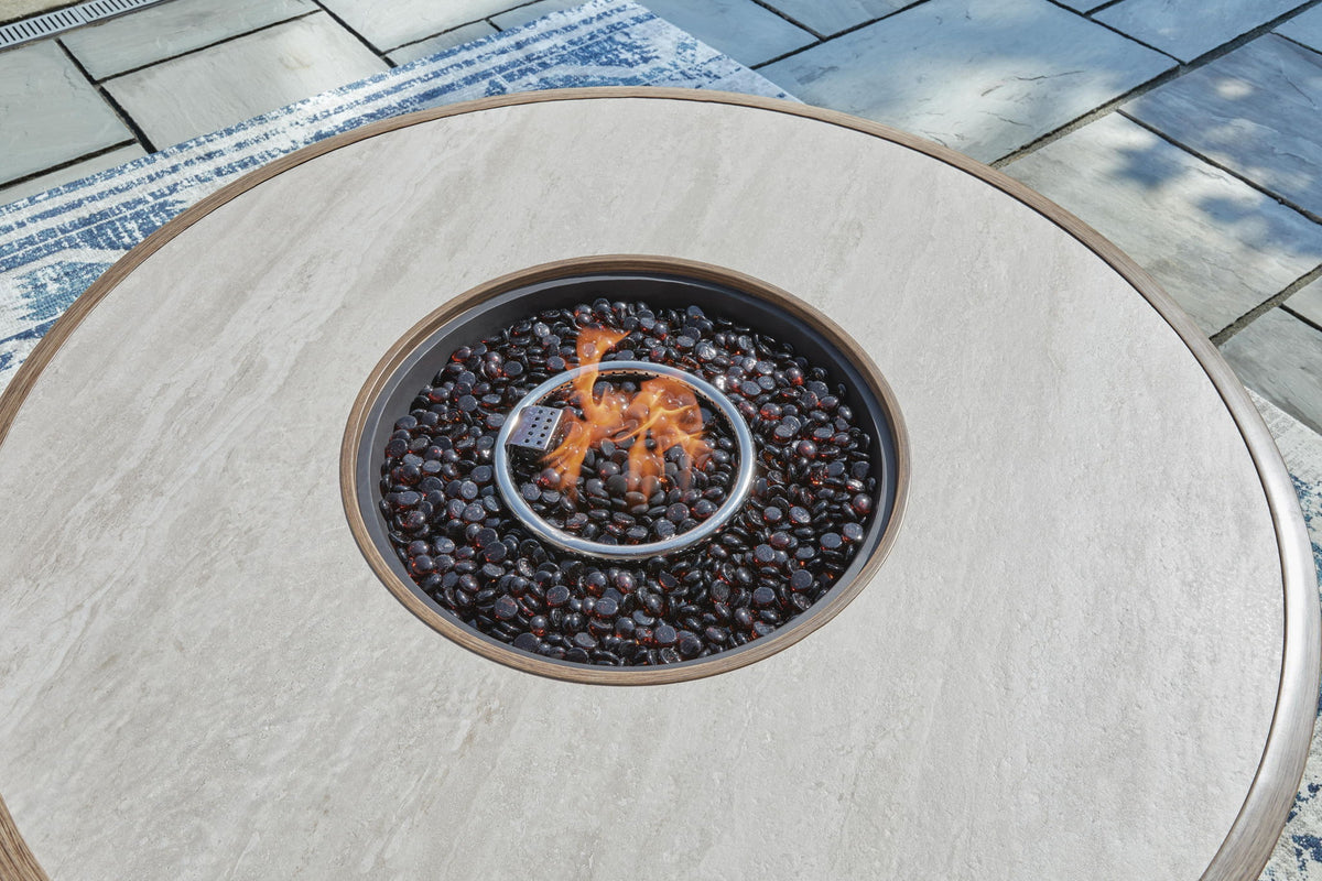 Beige Rainier Ranch round fire pit table by Signature Design Ashley, featuring a spacious tabletop and fire bowl for outdoor gatherings.