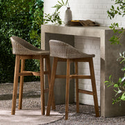 Noble House Beeson outdoor wicker and acacia wood barstool set in brown, water-resistant, with four stylish barstools arranged outside.