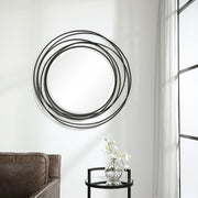 Uttermost Whirlwind round wall mirror with a sleek, modern frame hanging on a wall, reflecting light and surrounding decor.