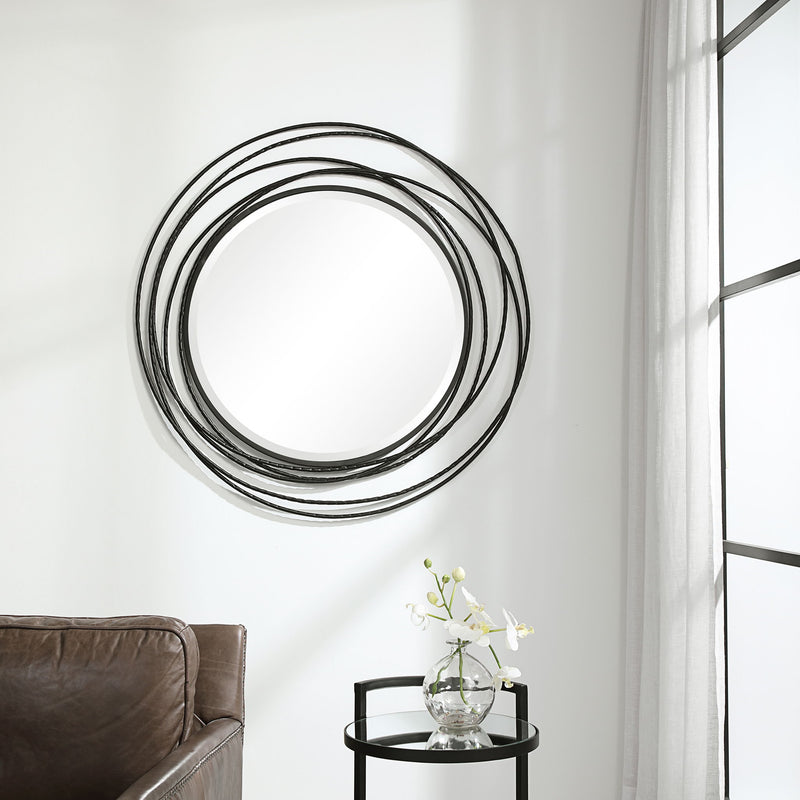 Uttermost Whirlwind round wall mirror with a sleek, modern frame hanging on a wall, reflecting light and surrounding decor.
