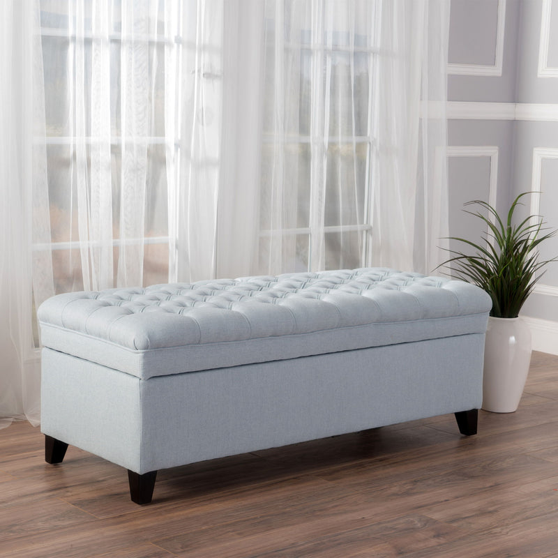 Noble House Juliana storage ottoman with beige fabric upholstery and birch wood legs, serving as a stylish storage and seating piece.