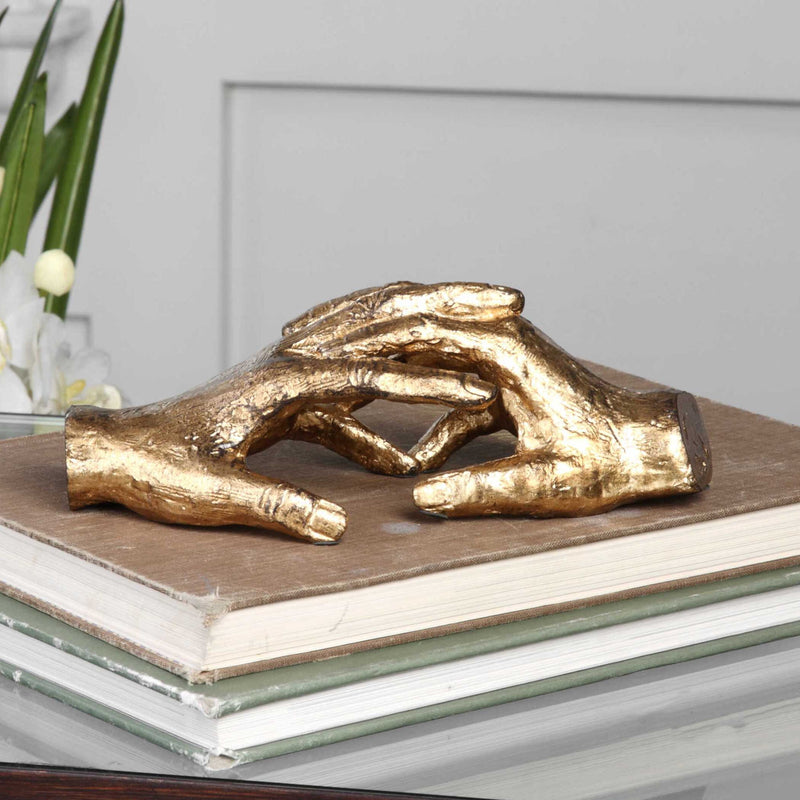 Gold "Hold My Hand" sculpture by Uttermost, featuring a detailed figurine capturing a heartfelt moment in a sleek design.